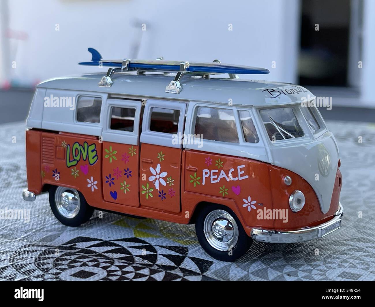 Nahaufnahme eines Modellautos des Volkswagen Minibusses mit einem Surfbrett auf dem Dach, Frieden und Liebe und Blumen auf der Seite Stockfoto