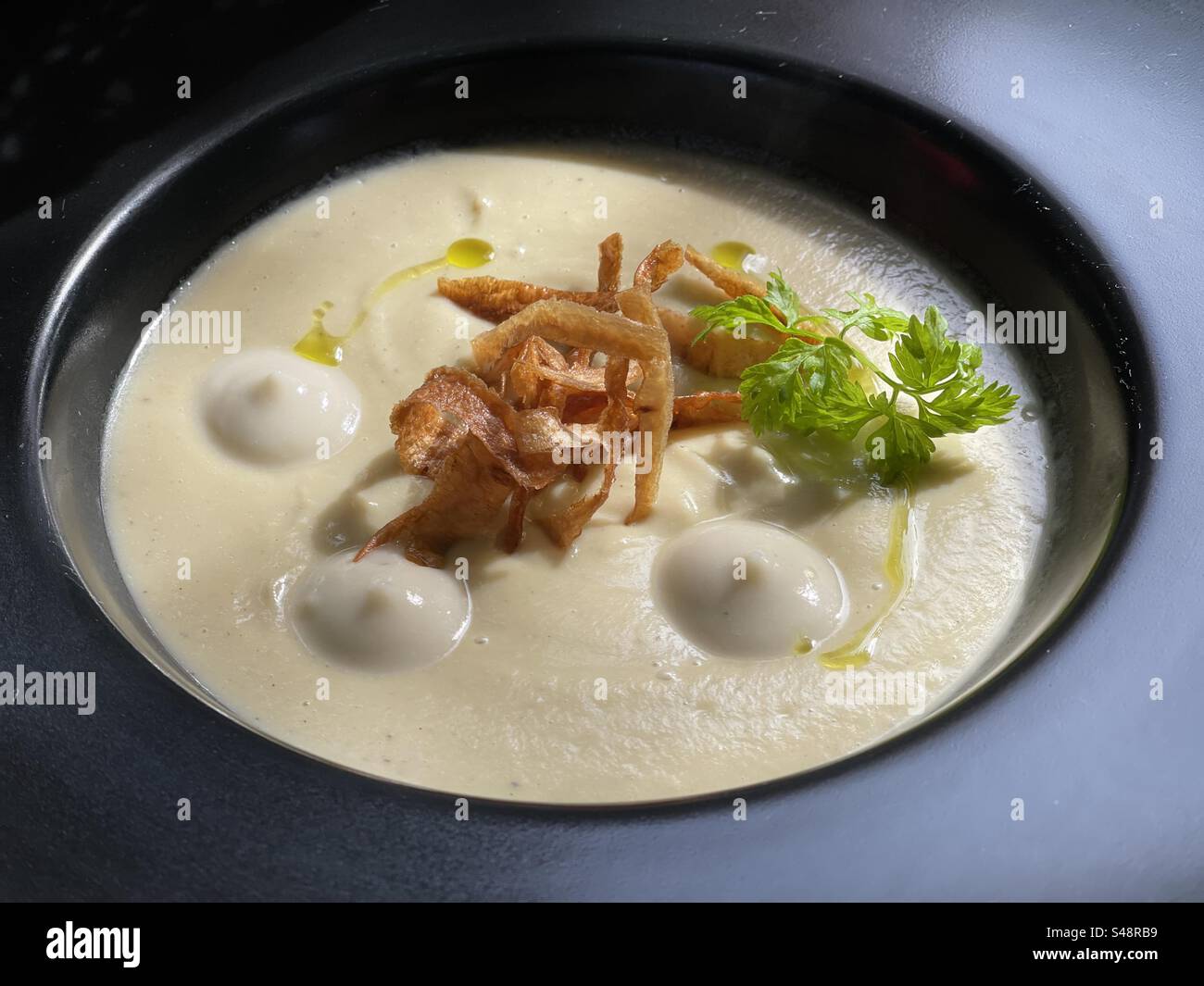 Nahaufnahme einer gastronomischen Blumenkohlsuppe mit Petersilie, dünnen frittierten Zwiebeln, Olivenöl auf einem schwarzen Restauranttteller in Montpellier, Occitanie, Frankreich Stockfoto
