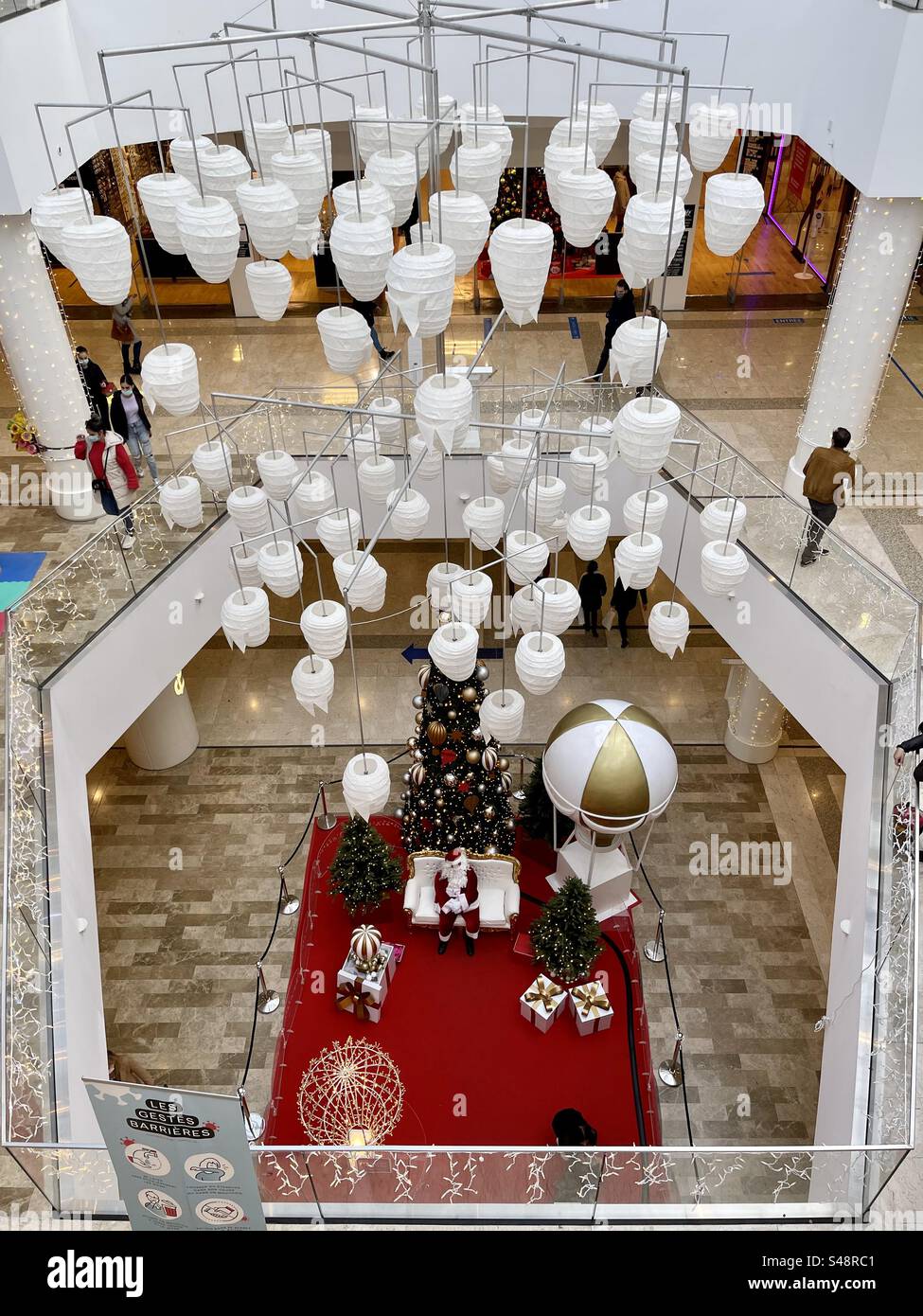 Innenaufnahme eines Einkaufszentrums, der Weihnachtsmann, der auf seinem Thron sitzt, umgeben von Weihnachtsschmuck und weißen Deckenleuchten während der Weihnachtszeit und COVID-Epidemien Stockfoto