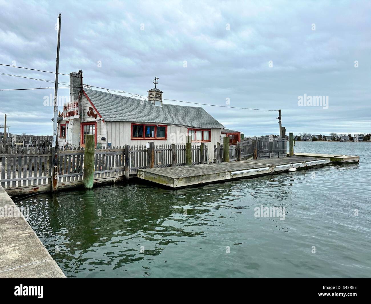 Clinton, Connecticut, USA: Außenansicht des Lobster Landing-Geschäfts an einem bewölkten Frühlingstag. Seitenansicht des Gebäudes mit Pier und Wasser. Fischrestaurant. - Smartphone-aufgenommenes Stockfoto