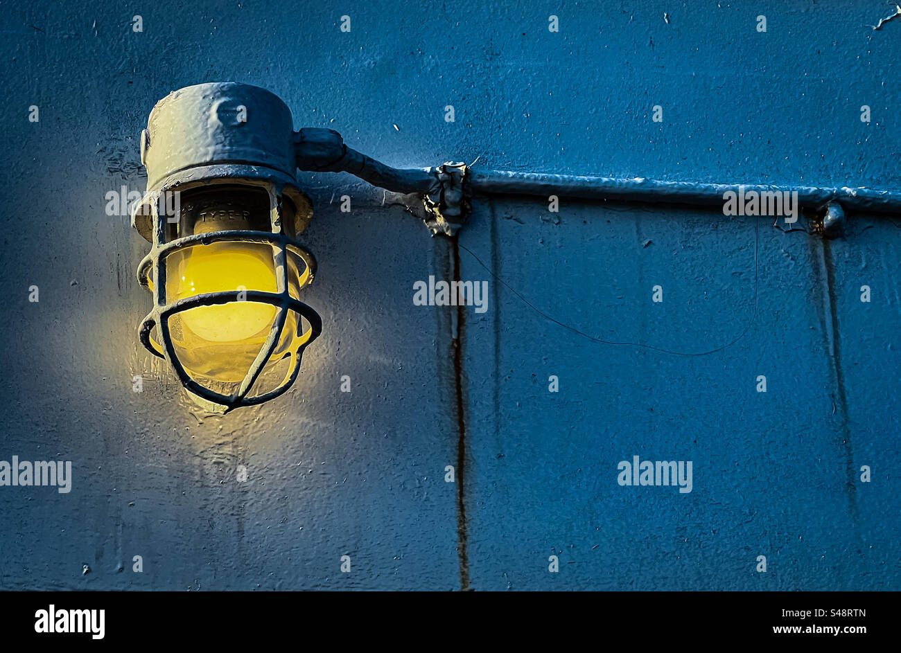 Leuchtendes Licht, das durch Metallkäfig an der Stahlschottwand von Booten geschützt wird - Smartphone-aufgenommenes Stockfoto
