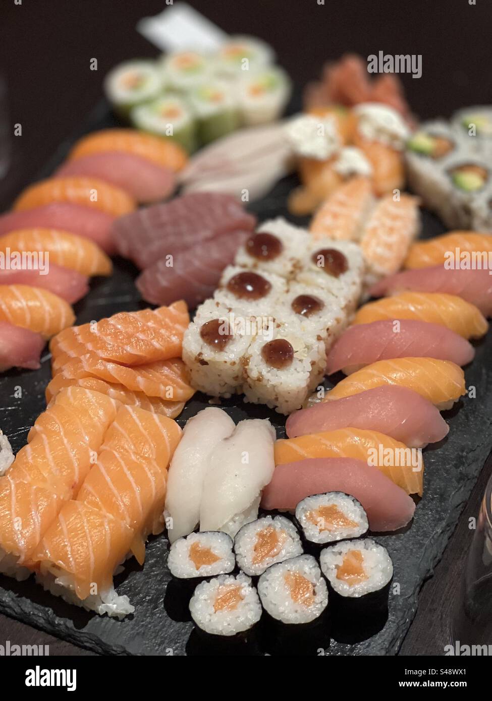 Nahaufnahme einer Black Box mit Sushi und Sashimi. Lachs, Thunfisch, Reis, Avocadobrötchen. Stockfoto