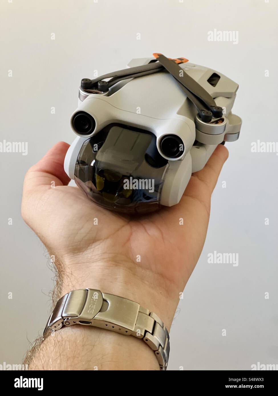 Studio-Aufnahme einer kleinen DJI Mini Pro 3 oder 4 Drohne auf einer Hand auf weißem Hintergrund. - Smartphone-aufgenommenes Stockfoto