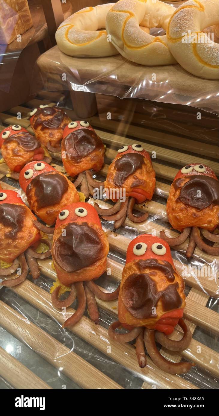 Entzückende Kraken-förmige Brötchen mit Schokoladenaugen und Tentakeln, kreativ gefertigt, um der Bäckerei einen verspielten, lustigen Touch zu verleihen. - Smartphone-aufgenommenes Stockfoto