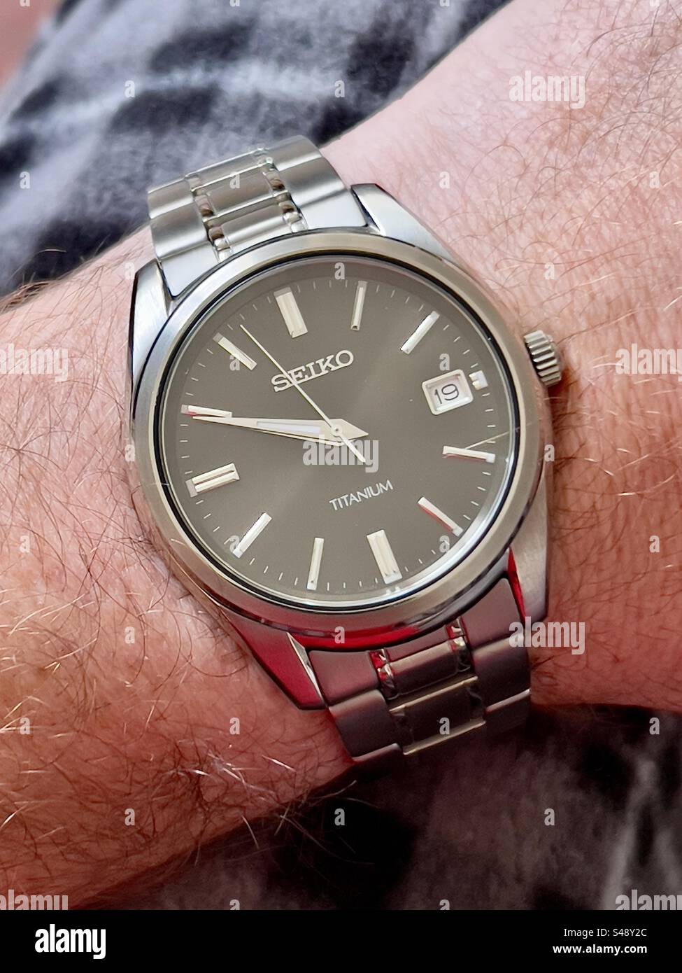 Nahaufnahme einer Seiko-Titankleiduhr auf dem Hintergrund einer karierten Hose. - Smartphone-aufgenommenes Stockfoto