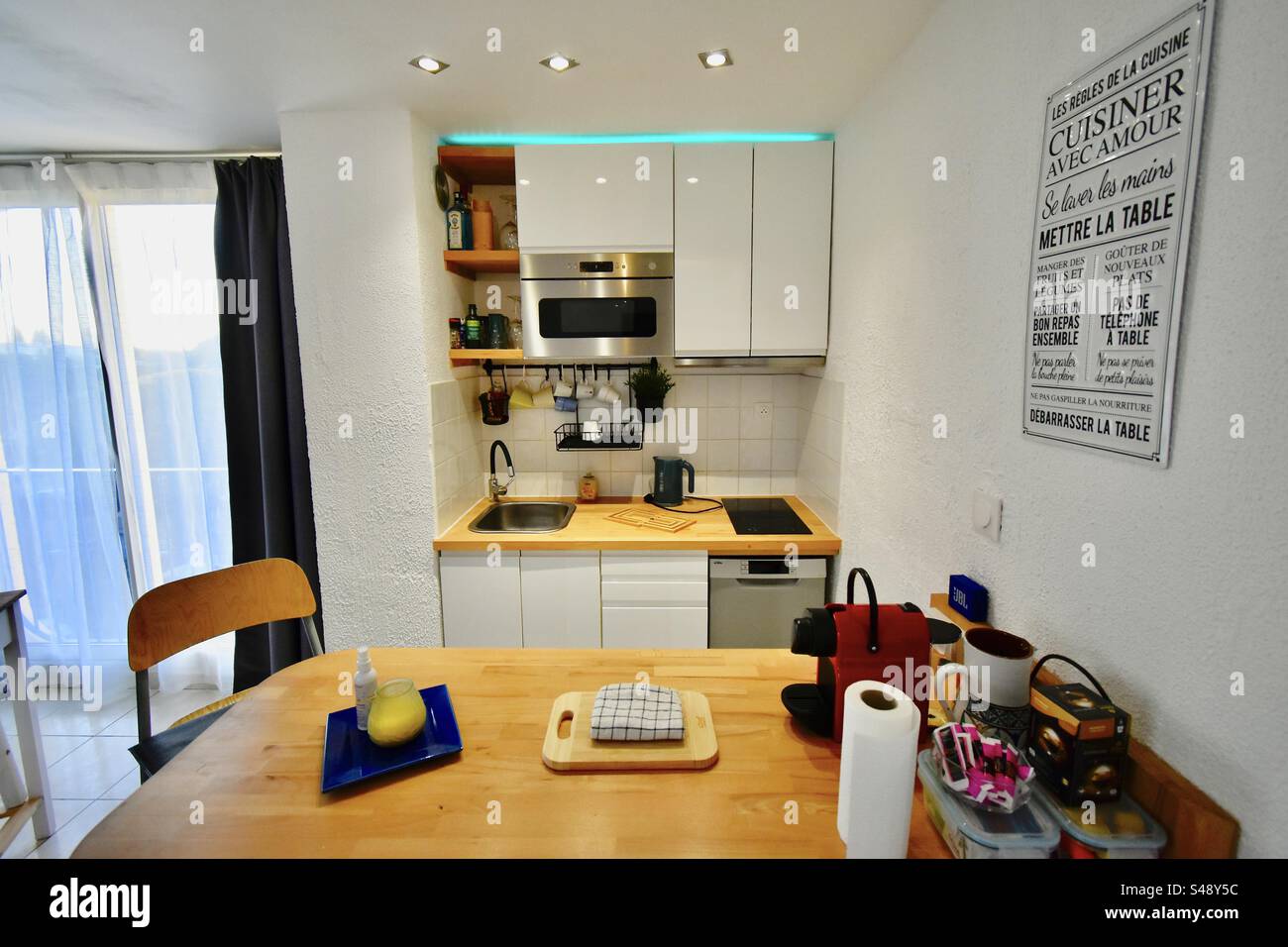 Breite Innenaufnahme einer kleinen offenen amerikanischen Küche mit Tisch und Stuhl, Accessoires, Papiertuch. Stockfoto