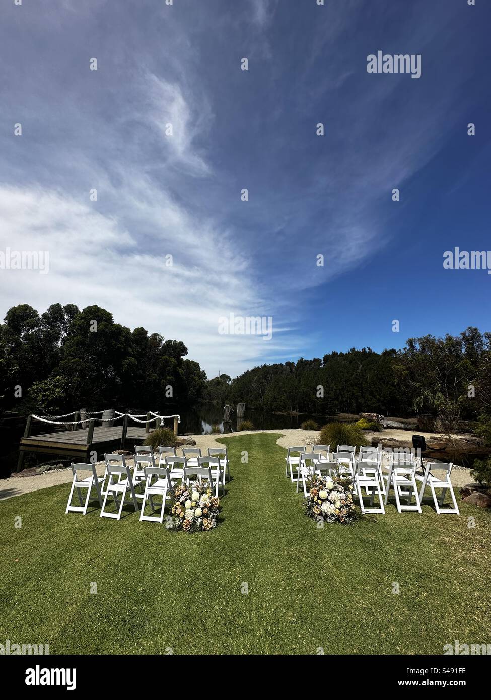 Hochzeitszeremonie am Fluss unter blauem Himmel. Hochzeitsblumen und Stühle für Gäste bereit für die Hochzeitszeremonie. Stockfoto