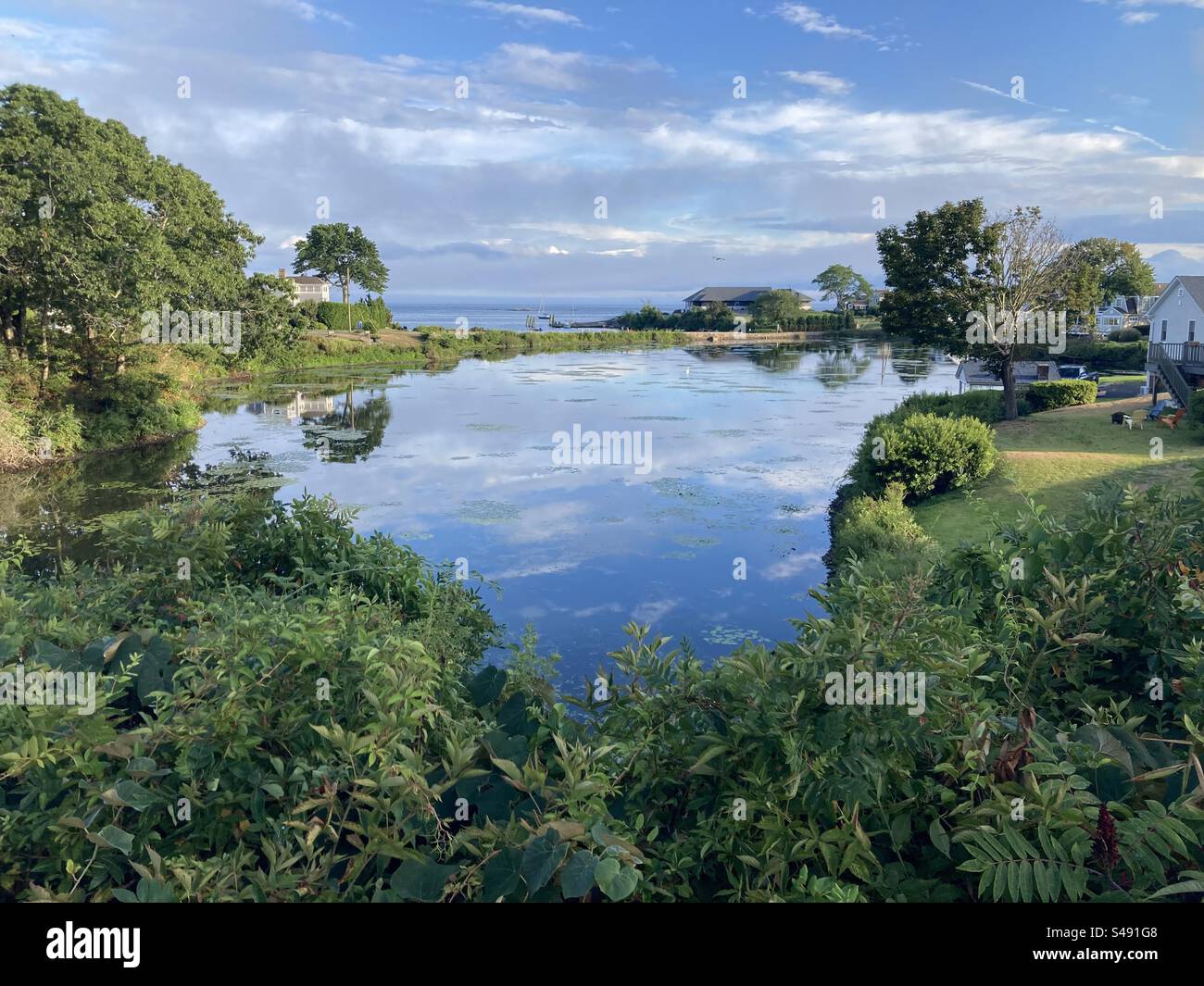 Blick auf den Teich in Niantic, Connecticut, USA an einem wunderschönen Tag mit dem Long Island Sound im Hintergrund. Reflexion von Wolken im Wasser. - Smartphone-aufgenommenes Stockfoto
