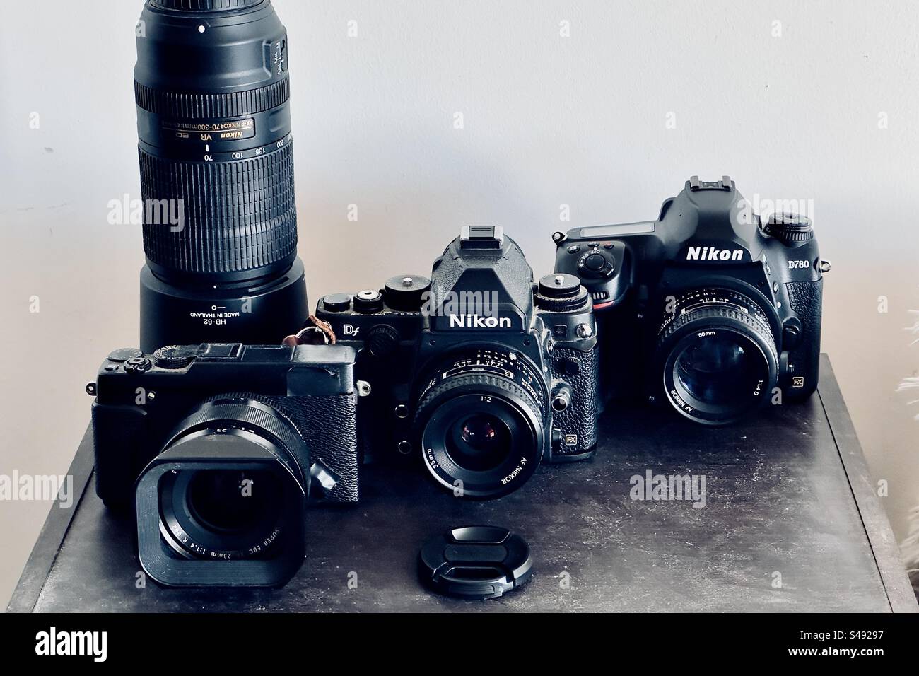 Studio-Aufnahme von drei Digitalkameras auf einem Holzregal. Ein mit Klebeband versehener Fujifilm X-E2s, ein Nikon DF und ein Nikon D780 mit verschiedenen Objektiven und Teleobjektiven. Stockfoto