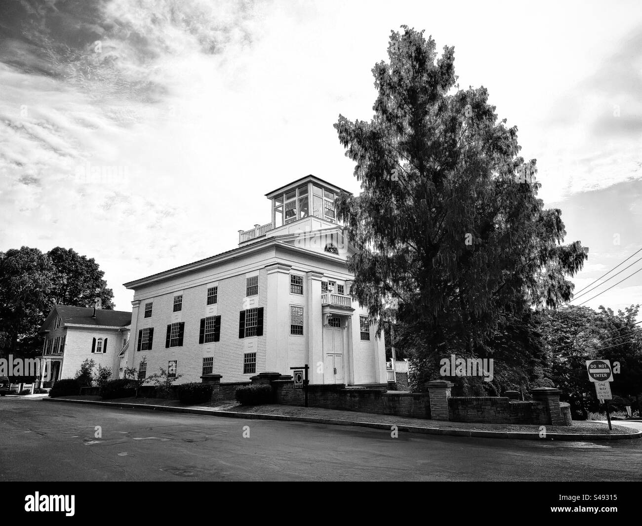 Weißes Holzgebäude in Essex, Connecticut, USA, mit Glasturm. Sehr, großer Baum direkt daneben. Schwarzweißfilter. - Smartphone-aufgenommenes Stockfoto