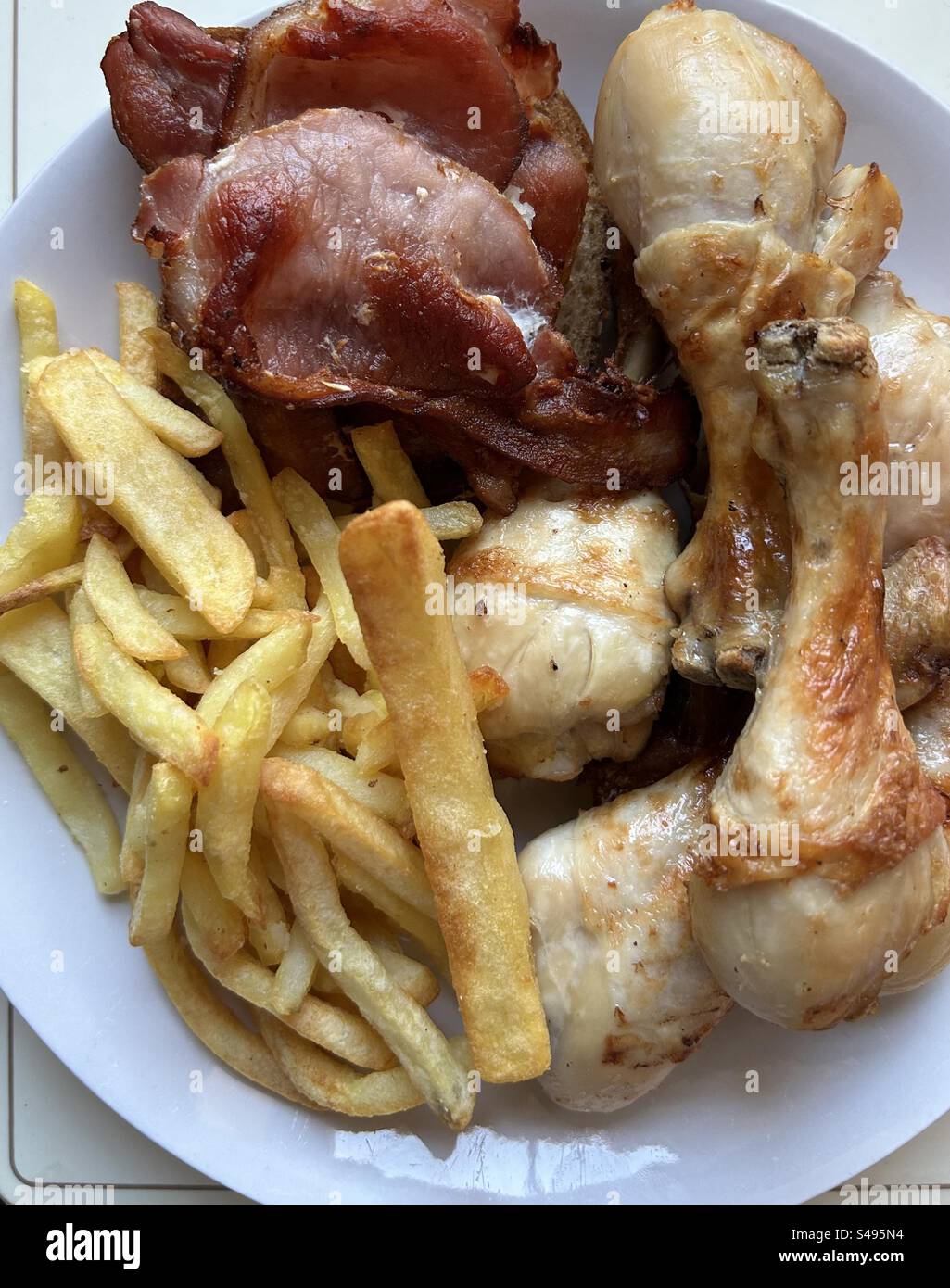 Hähnchenkeulen mit knusprigem Speck und Pommes frites braten. - Smartphone-aufgenommenes Stockfoto