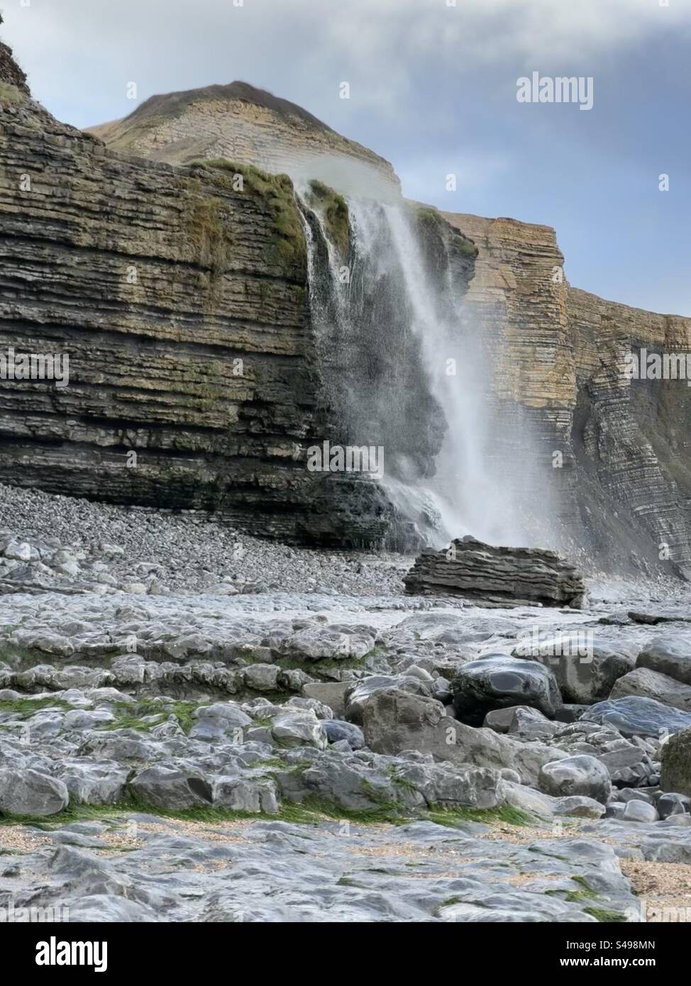 Wasserfall, während Nant Cwm Mawr über Klippen auf Traeth Mawr, Glamorgan Heritage Coast, Südwales stürzt, mit Wind, der das Wasser bergauf weht. Stockfoto