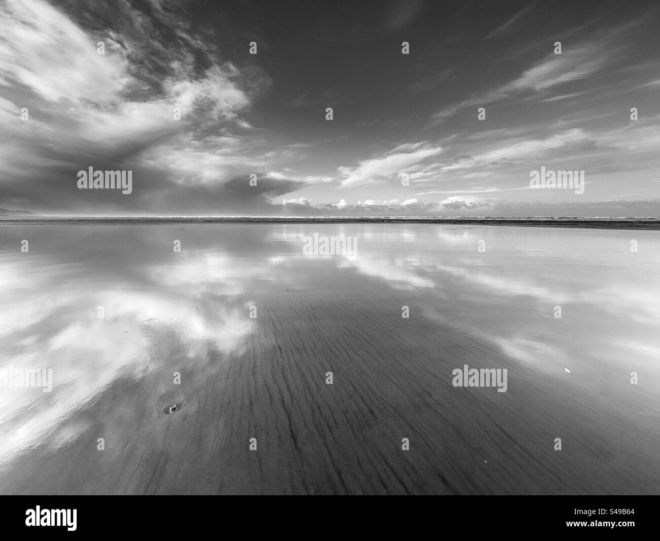 Der Morgenhimmel spiegelt sich bei Ebbe am Strand Stockfoto