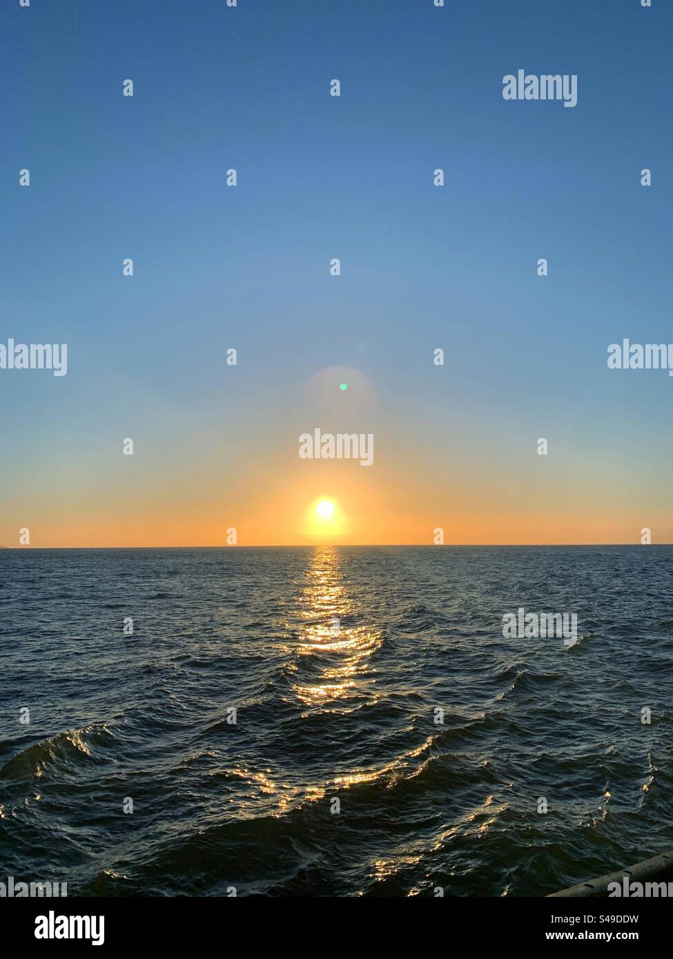 Sonnenuntergang auf dem Meer. Nichts als Wasser, wo man hinsieht. Die Sonne geht über dem ruhigen Wasserhorizont unter. Stockfoto