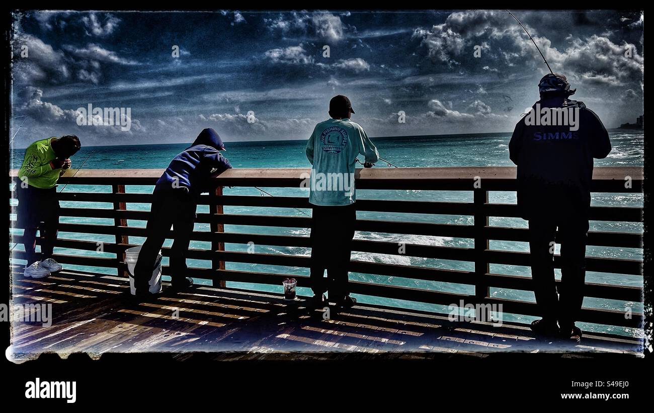 Männer fischen am Juno Beach am Juno Pier in Jupiter, Florida, USA an einem sonnigen warmen, wenn auch teilweise bewölkten Tag im Januar. Stockfoto