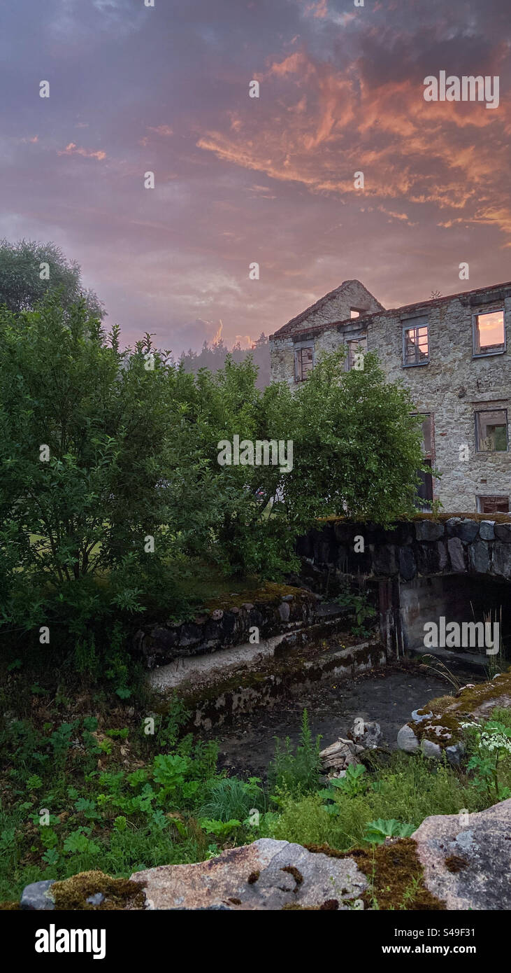 Vaives dzirnavas Mühle - verlassene Mühle in Lettland an einem teilweise sonnigen Abend kommt Regen, aber die Wolken sind rot wegen der niedrigen Sommersonne. Stockfoto