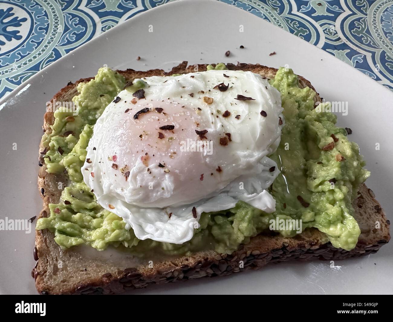 Pochiertes Ei mit roten Pfefferflocken auf Avocadotoast zum Frühstück. Stockfoto