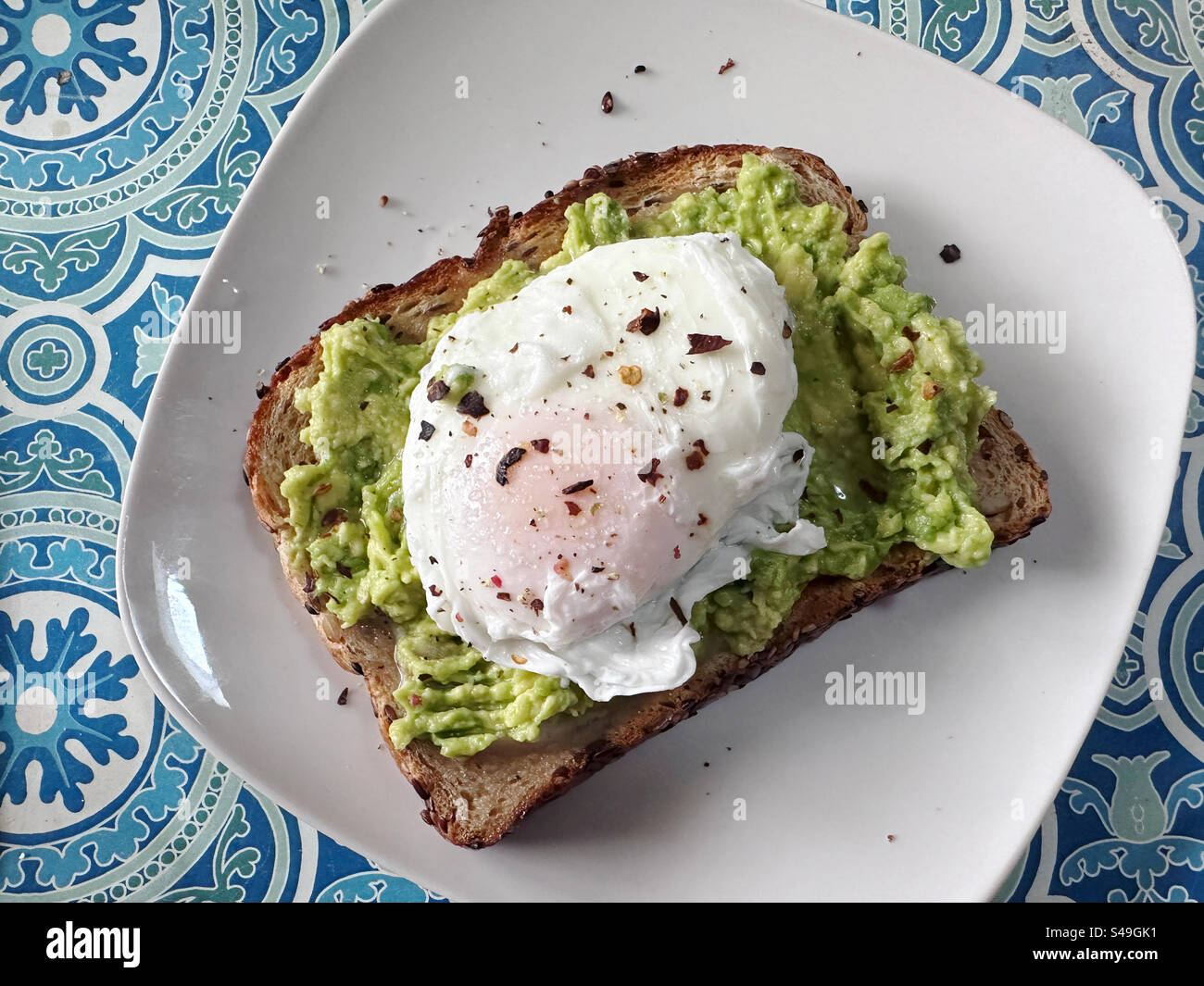 Ein pochiertes Ei mit roten Pfefferflocken auf Avocadotoast zum Frühstück. Stockfoto