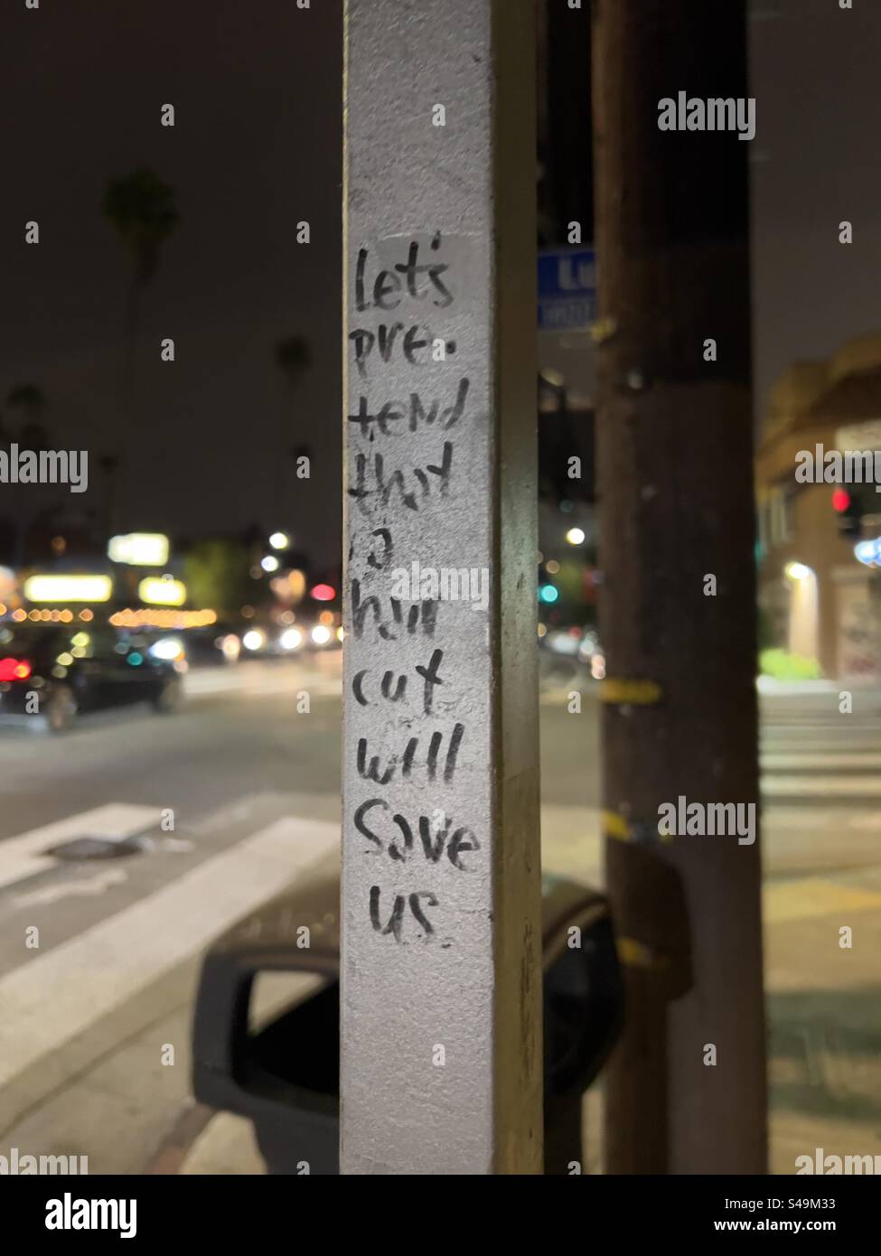 LOS ANGELES, CA, JUN 2023: Graffiti auf einem Metallpfosten in der Straße bei Nacht: 'Lasst uns so tun, als ob ein Haarschnitt uns retten wird.' Foto im Hochformat Stockfoto