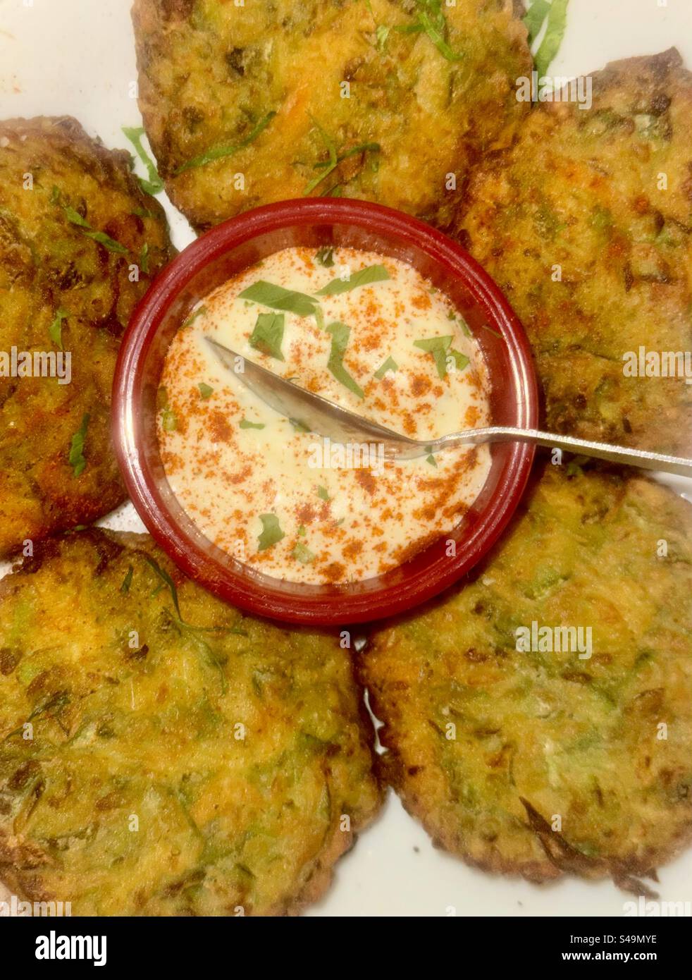 Traditionelle griechische Vorspeise mit Zucchini-Krapfen (Kolokithokeftedes) serviert mit einem cremigen Joghurtdip. - Smartphone-aufgenommenes Stockfoto