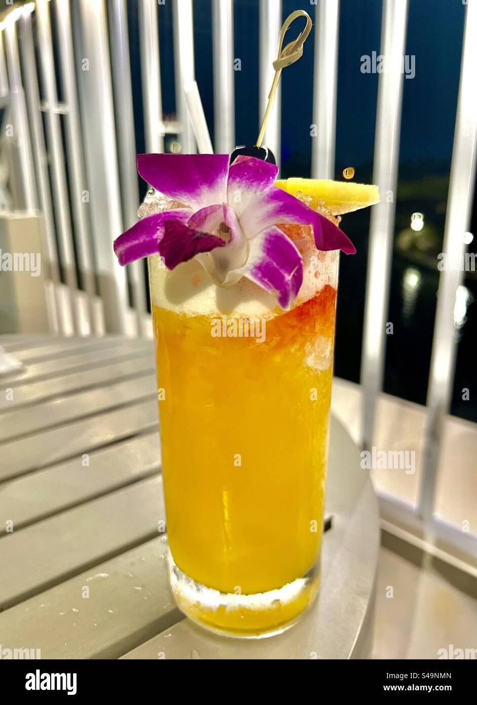 Leuchtend orangefarbenes tropisches Getränk für Erwachsene mit violetter und weißer Orchidee - Smartphone-aufgenommenes Stockfoto