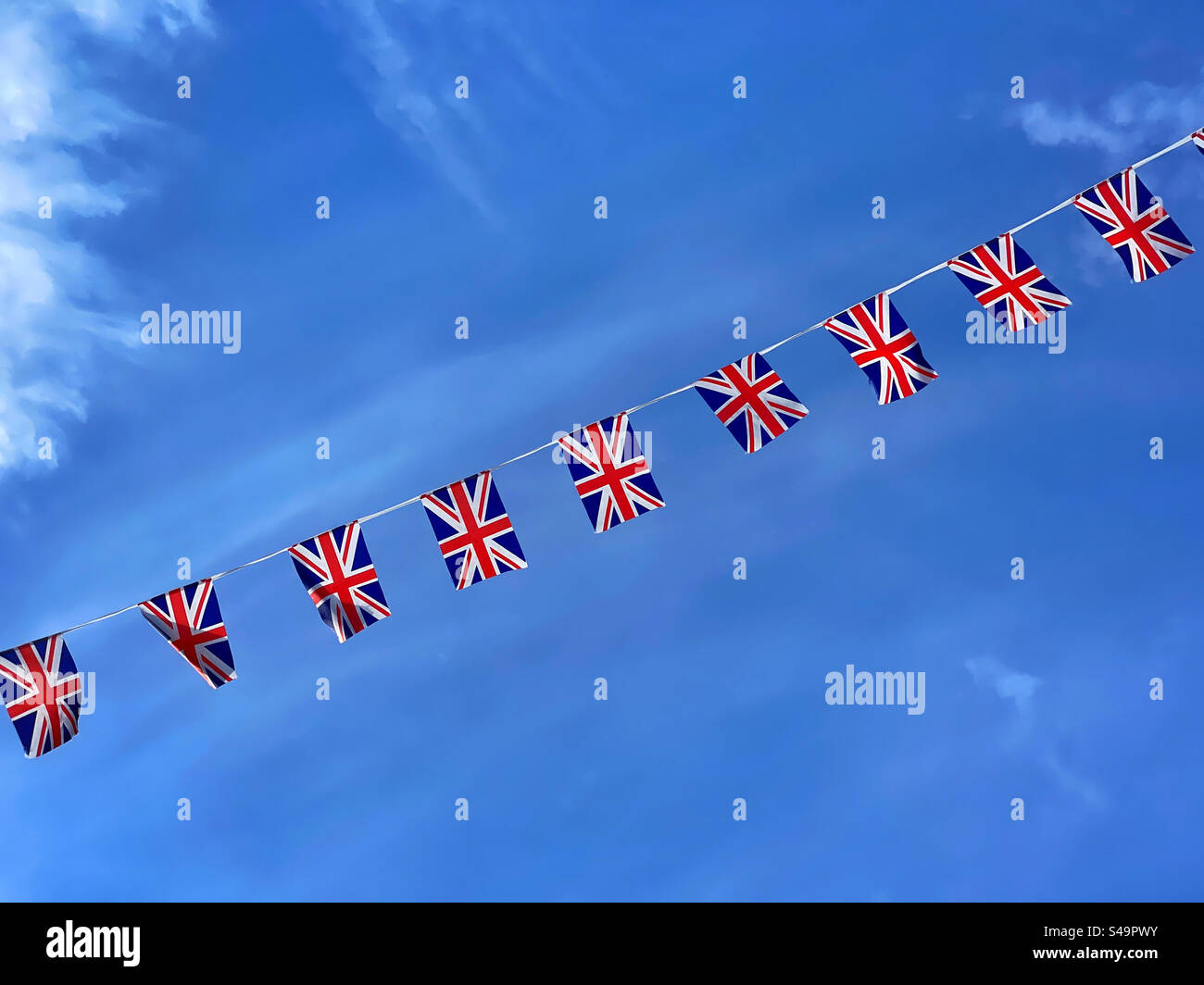 Union Jack Fahnen flattern an einem Sommertag im Vereinigten Königreich in einem blauen Himmel. Schöne Beleuchtung, Texturen und Kopierraum. Foto ©️ COLIN HOSKINS. Stockfoto