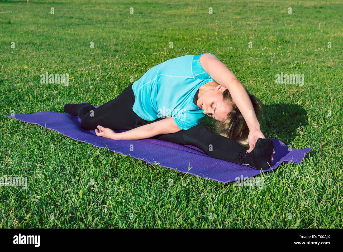 Lustiges Foto über junge Frau Yoga Übung mit lustigen Grimasse. Fitness Mädchen mit einem Smartphone auf Natur Hintergrund, genießt die sportliche Ausbildung, wor Stockfoto