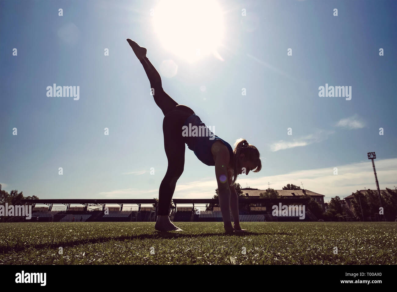 Junge schlanke blonde Frau am grünen Rasen des Stadions am Morgen die Übungen. Mädchen One-Legged Downward-Facing Hund darstellen. Gesunde Lebensweise überbieten Stockfoto