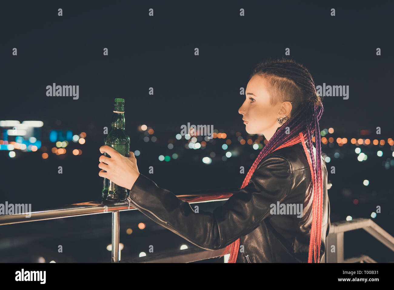 Punk Mädchen erhält betrunken auf dem Hintergrund eines hohen Gebäudes auf dem Hintergrund einer unscharfen Nacht Stadt. Nachdenkliche traurige Ausdruck. unglücklich, Emotion. Stockfoto