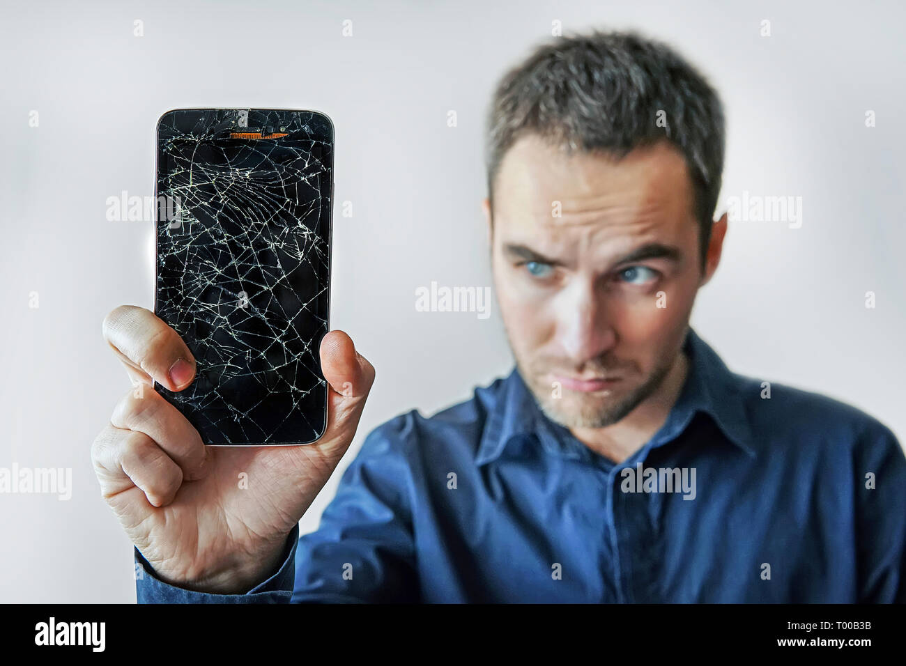 Traurige Mann hält gebrochen Smartphone. Bildschirm defekt. Nicht funktionierendes Telefon Stockfoto