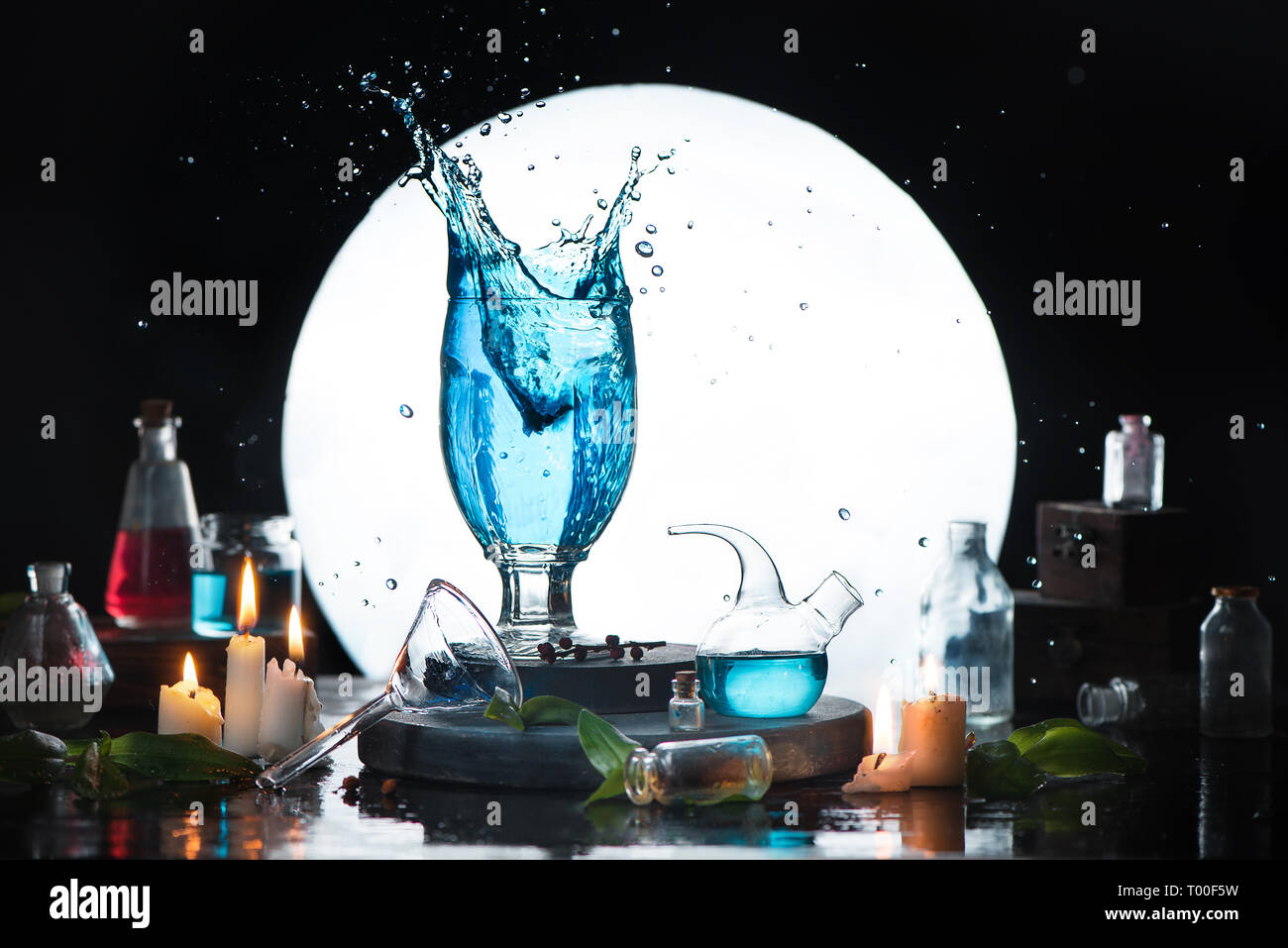Becher mit einem magischen Trank in Hexe, Zauberer oder alchemisten Arbeitsplatz mit Labor Glas, Kräuter und Full Moon Silhouette. High Speed Fotografie Stockfoto