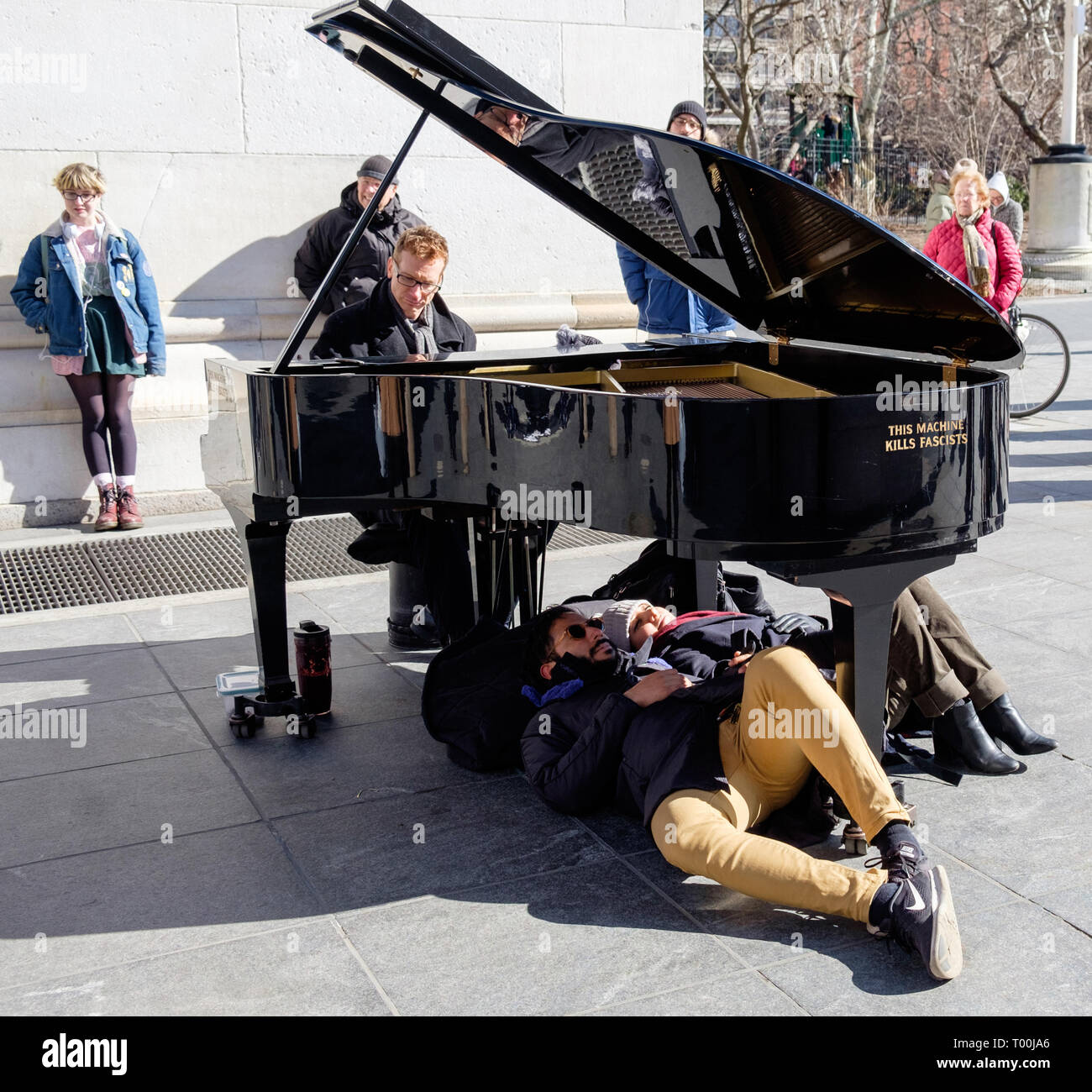 Colin Huggins spielt Klavier mit "Diese Maschine tötet Faschisten" & 2 Personen unter am Washington Square Park, Greenwich Village, Mar 2018 zur Festlegung Stockfoto
