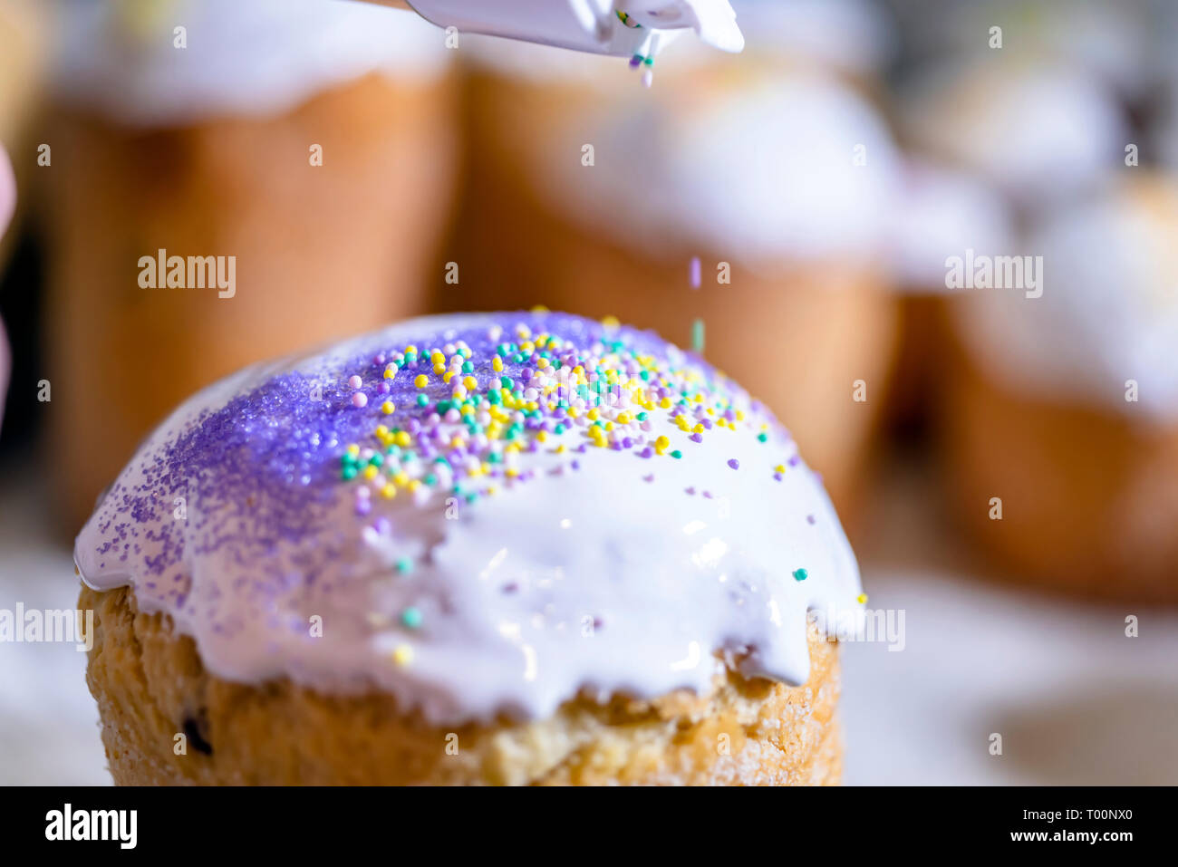 Baker schmückt den oberen Teil von Ostern Kuchen mit weißen Zucker durch farbige Kristallzucker gießen Dekoration auf frisch Puderzucker Puderzucker bedeckt, tra Stockfoto