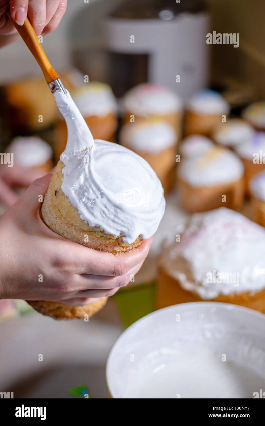 Ein Bäcker Bürsten eine flüssige Schlagsahne Zuckerguss auf der Spitze eines traditionellen Ostern Kuchen aus der Konditorei zubereitet und gebacken in zylindrische Formen der t zu verzieren Stockfoto