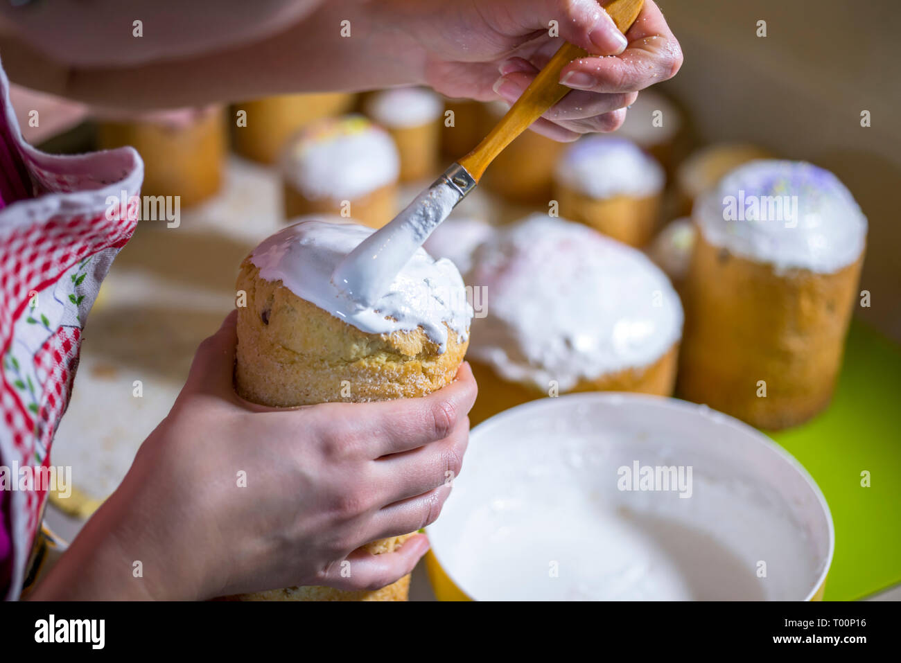 Ein Bäcker Bürsten eine flüssige Schlagsahne Zuckerguss auf der Spitze eines traditionellen Ostern Kuchen aus der Konditorei zubereitet und gebacken in zylindrische Formen der t zu verzieren Stockfoto