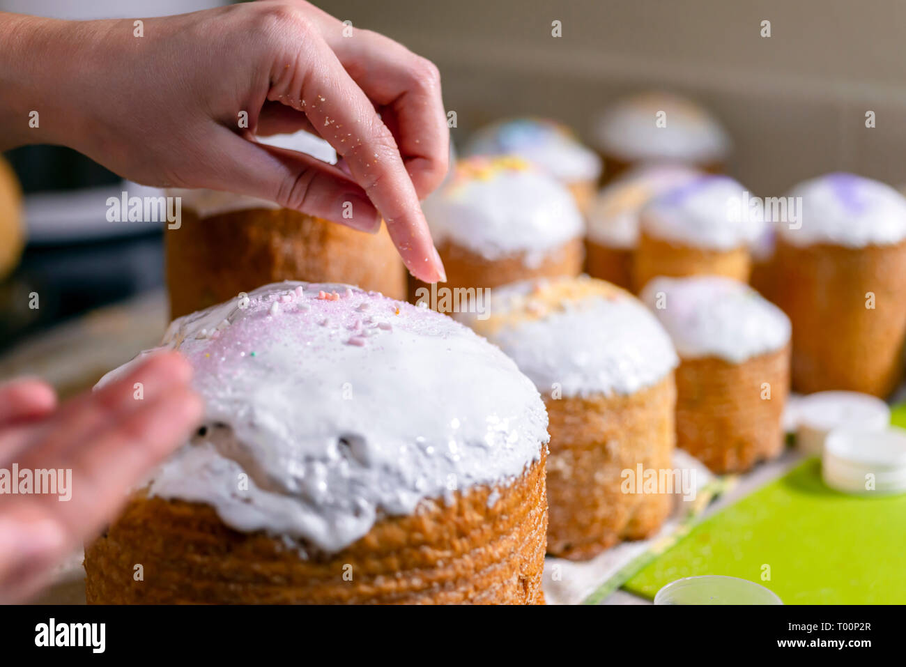 Baker schmückt den oberen Teil von Ostern Kuchen mit weißen Zucker durch farbige Kristallzucker gießen Dekoration auf frisch Puderzucker Puderzucker bedeckt, tra Stockfoto