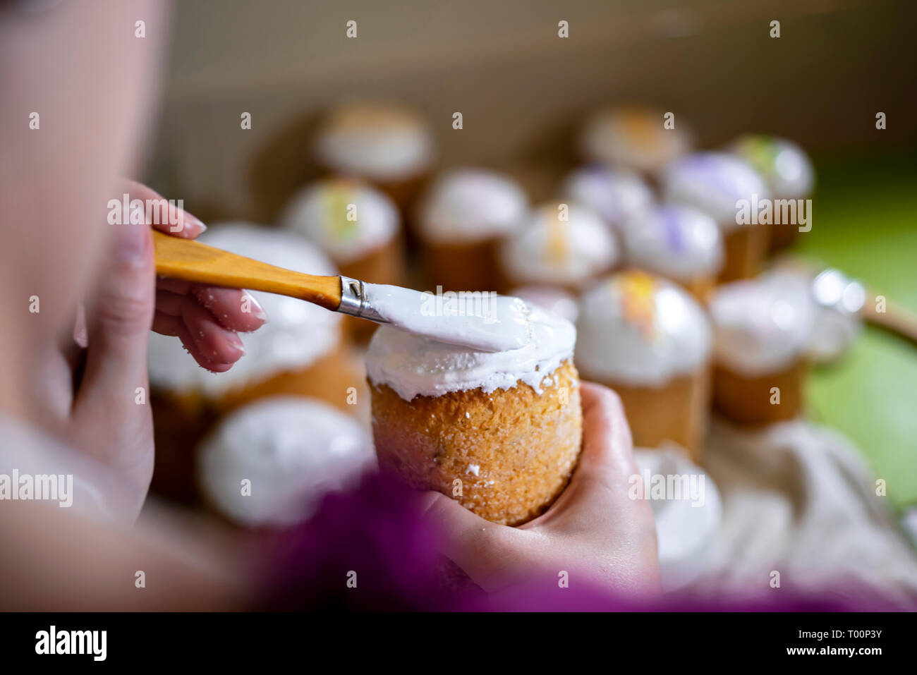 Ein Bäcker Bürsten eine flüssige Schlagsahne Zuckerguss auf der Spitze eines traditionellen Ostern Kuchen aus der Konditorei zubereitet und gebacken in zylindrische Formen der t zu verzieren Stockfoto