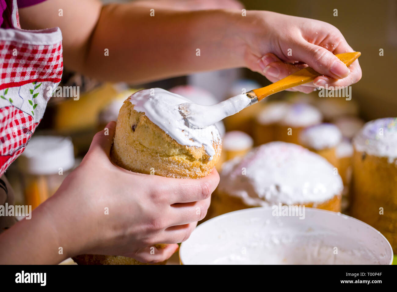 Ein Bäcker in Schürze Bürsten eine flüssige Schlagsahne Zuckerguss auf der Oberseite der traditionellen Ostern Kuchen aus der Konditorei zubereitet und gebacken in zylindrische Formen zu decorat Stockfoto
