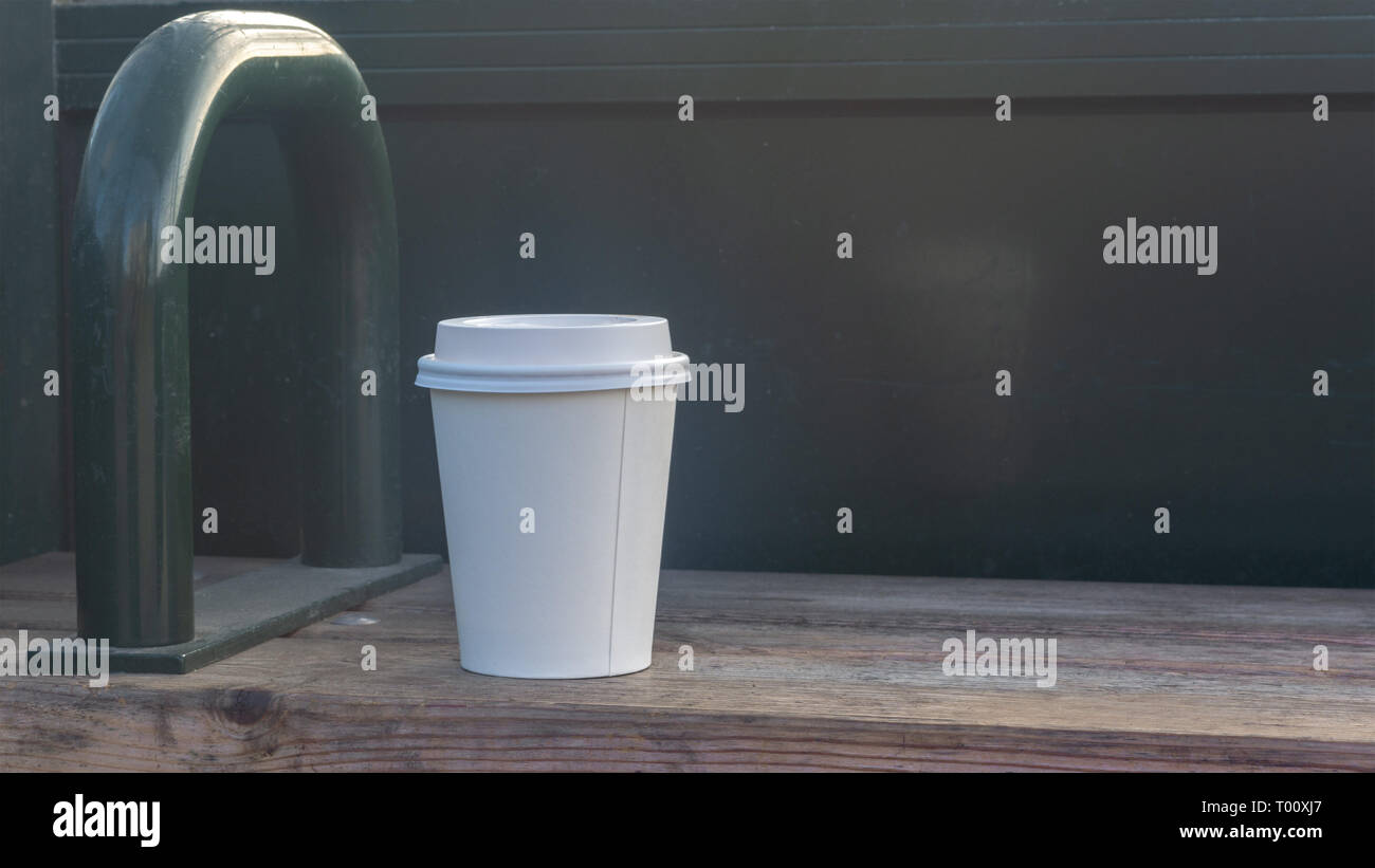 Weißes Glas mit Deckel für Kaffee an einer Bushaltestelle. Kopieren Sie Platz Stockfoto