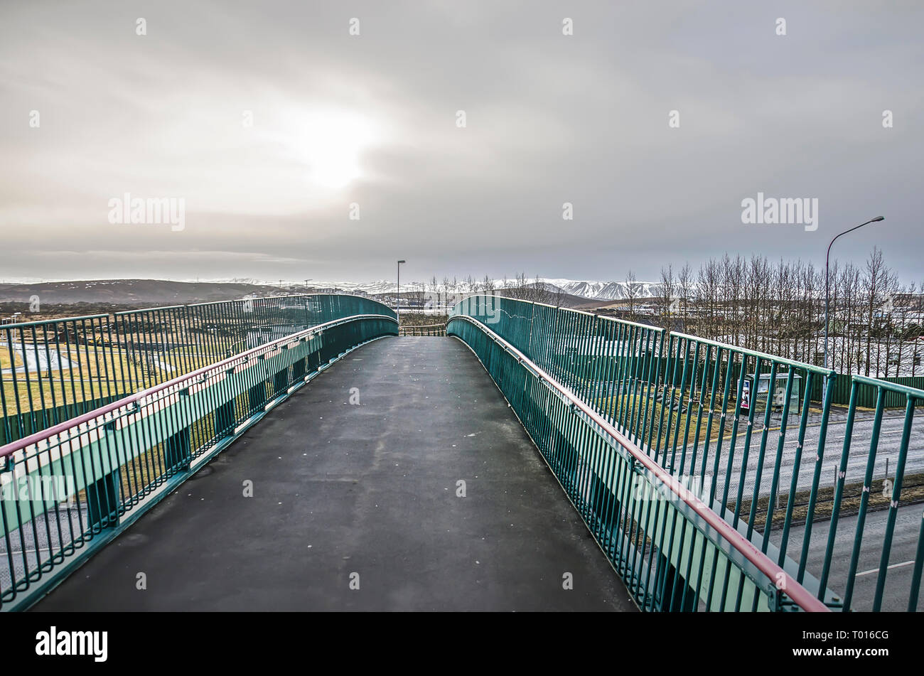 Fußgänger- und Fahrrad Brücke mit einer Asphaltdecke über eine Autobahn in der Nähe von Reykjavik, Island unter einem bewölkten Himmel Stockfoto