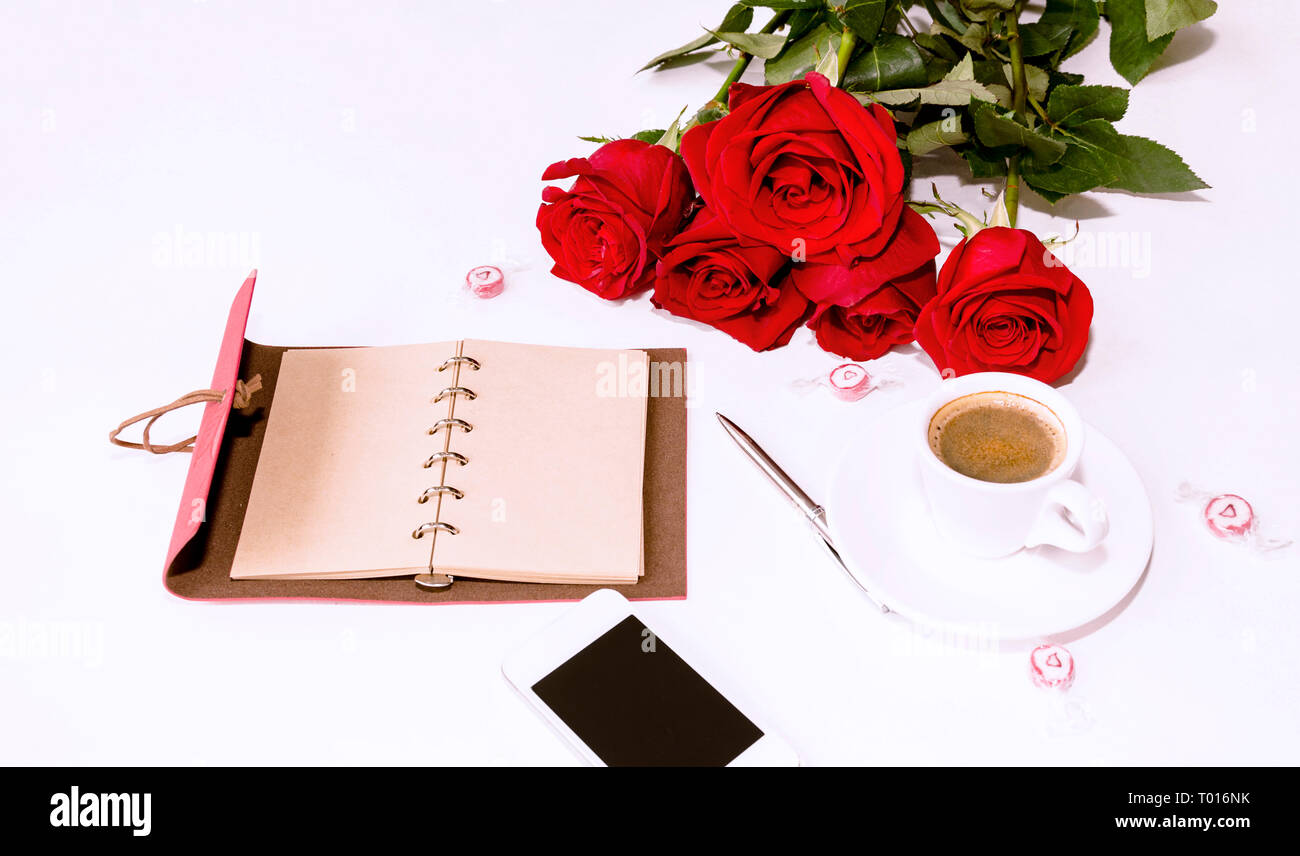Notebook mit einem Stift, ein Telefon und ein Strauß roter Rosen, Süßigkeiten und einer Tasse Kaffee auf einen hellen Hintergrund Stockfoto