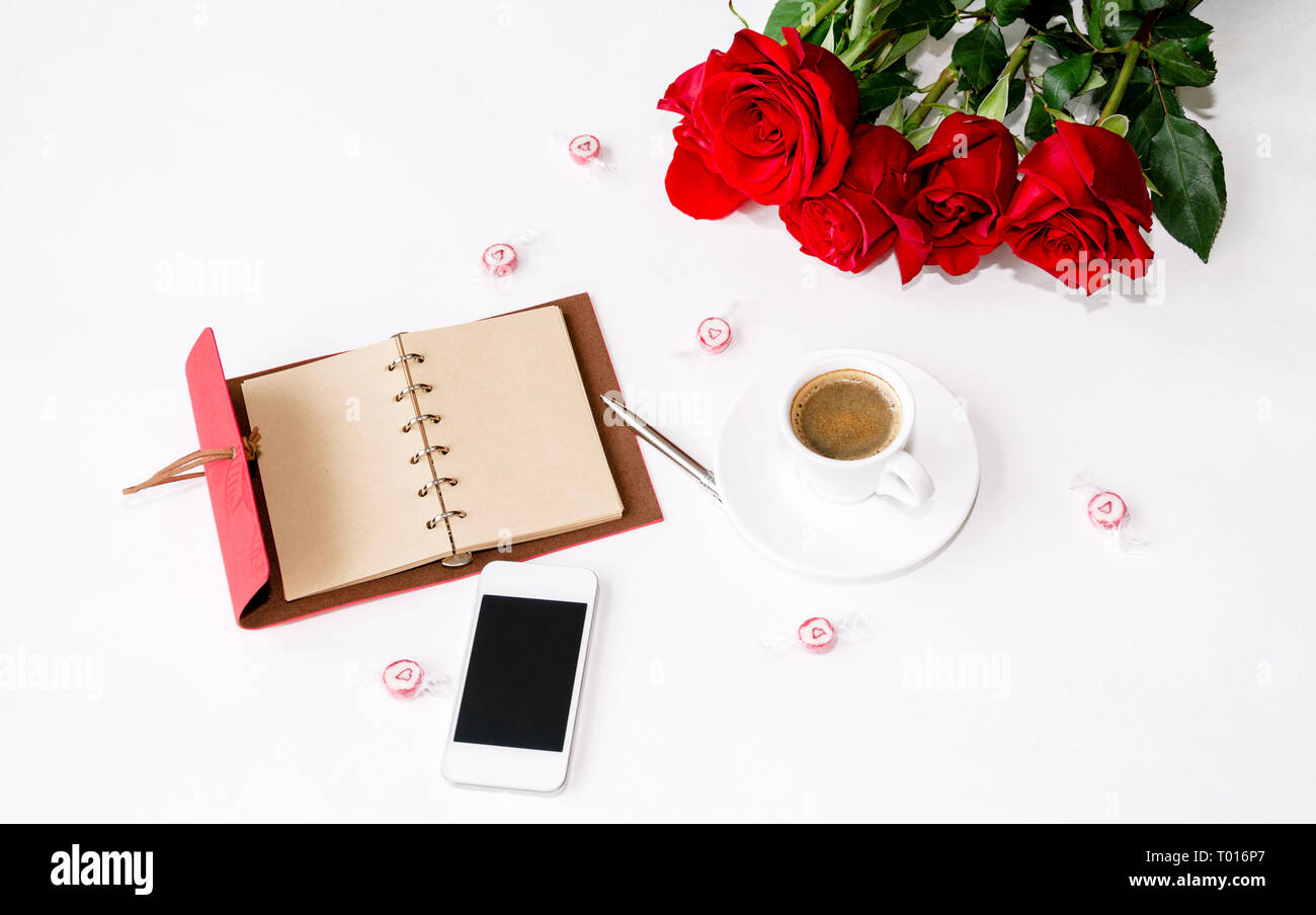 Notebook mit einem Stift, ein Telefon und ein Strauß roter Rosen, Süßigkeiten und einer Tasse Kaffee auf einen hellen Hintergrund Stockfoto