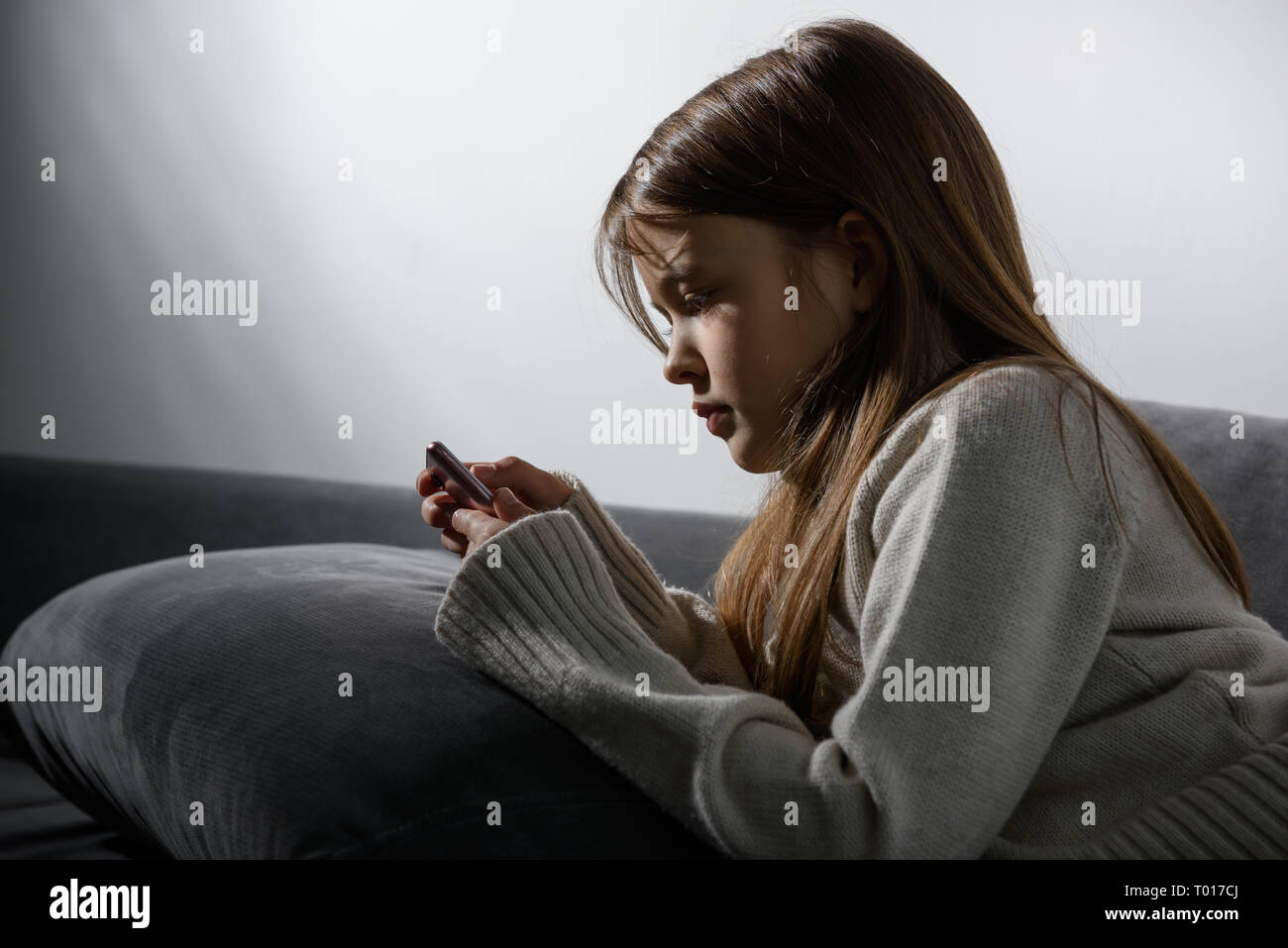 Das junge Mädchen ist auf den Bildschirm eines Smartphones lehnte sich auf dem Sofa mit Kissen. Stockfoto