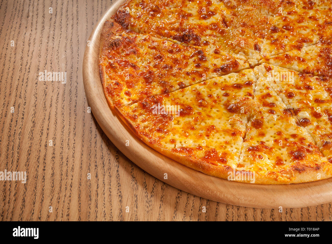 Pizza mit Käse heiß serviert und lecker auf Holzplatte auf Tisch. Schnelle und kostengünstige Mahlzeit Stockfoto