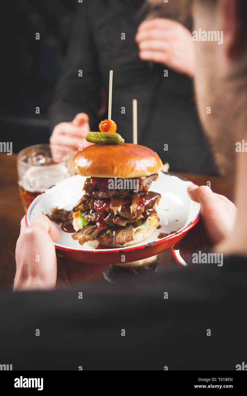 Ein Kellner serviert eine schmierige Beef Burger auf einer metallischen Platte, die in einem Restaurant Stockfoto
