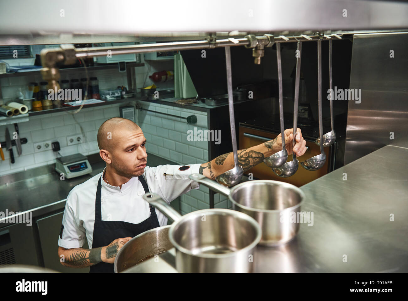 Kochen Suppe. Junge männliche Koch im Vorfeld der Wahl einer Schöpfkelle für seine berühmten Suppe, während in einem Restaurant in der Küche stehen. Kochen Konzept Stockfoto