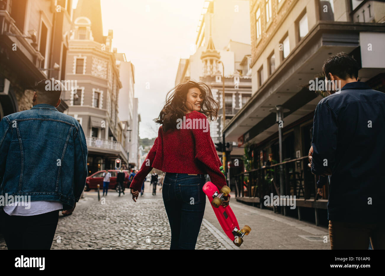 Ansicht von hinten mit einem lächelnden Asiatin zurück drehen mit einem Skateboard auf Straße der Stadt. Fröhliche Frau zu Fuß draußen mit ihren Freunden. Stockfoto