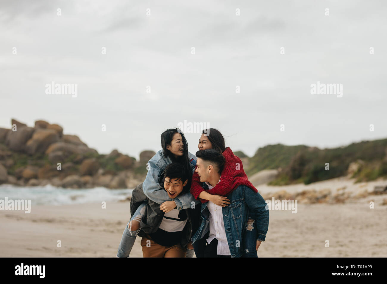 Junge asiatische Männer, die Frauen, die Freunde auf dem Rücken am Strand. Gruppe von Freunden huckepack draußen auf dem Meer. Stockfoto