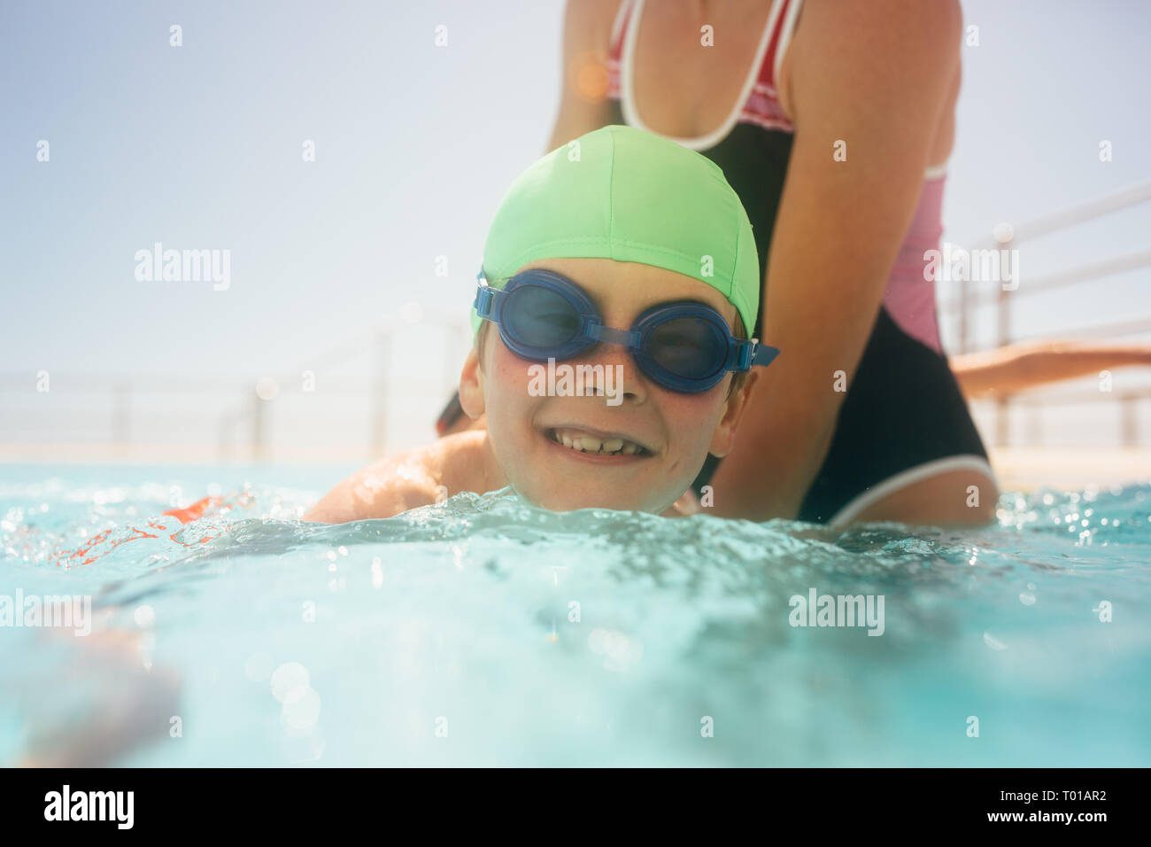 Cute boy tragen Badekappe und Schutzbrille lernen mit einer Frau, die Hilfe in einem Pool zu schwimmen. Junge in Schwimmunterricht im Pool mit dem Trainer. Stockfoto