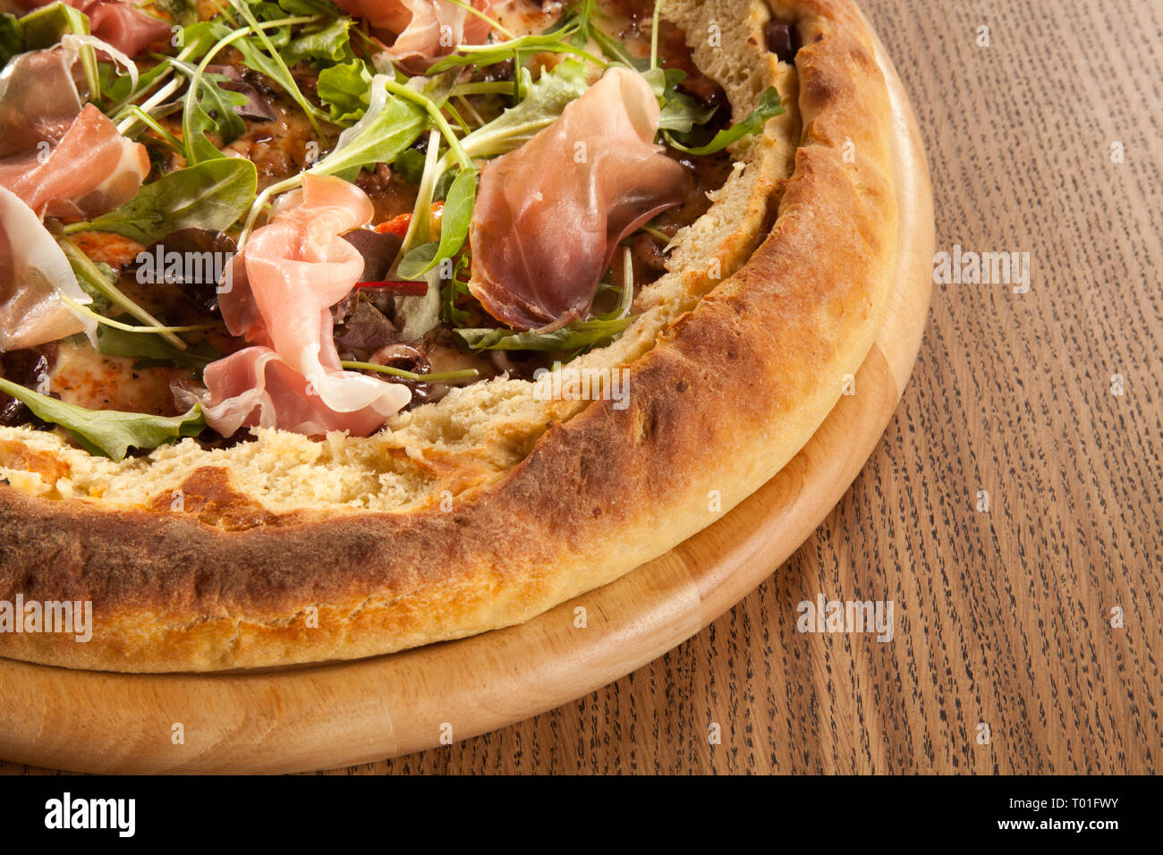 Pizza mit Speck und Vegetation serviert auf hölzernen Platte mit Petersilie Salat grüne Fleisch und Käse Stockfoto
